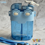 A dual-compartment translucent azure-blue water bottle wrapped in a sky-blue silicone shoulder sleeve with two rounded cream push buttons, topped by dual dark blue translucent lids with a tiny 3D Cinnamoroll figure resting on one side, shown with a matching blue character strap
