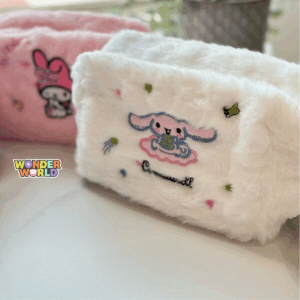 A close-up shot of a fluffy, cloud-white plush makeup pouch decorated with detailed embroidery of Cinnamoroll sitting on a pink cloud and sipping from a green teacup, surrounded by tiny embroidered stars and candies, with cursive character branding below