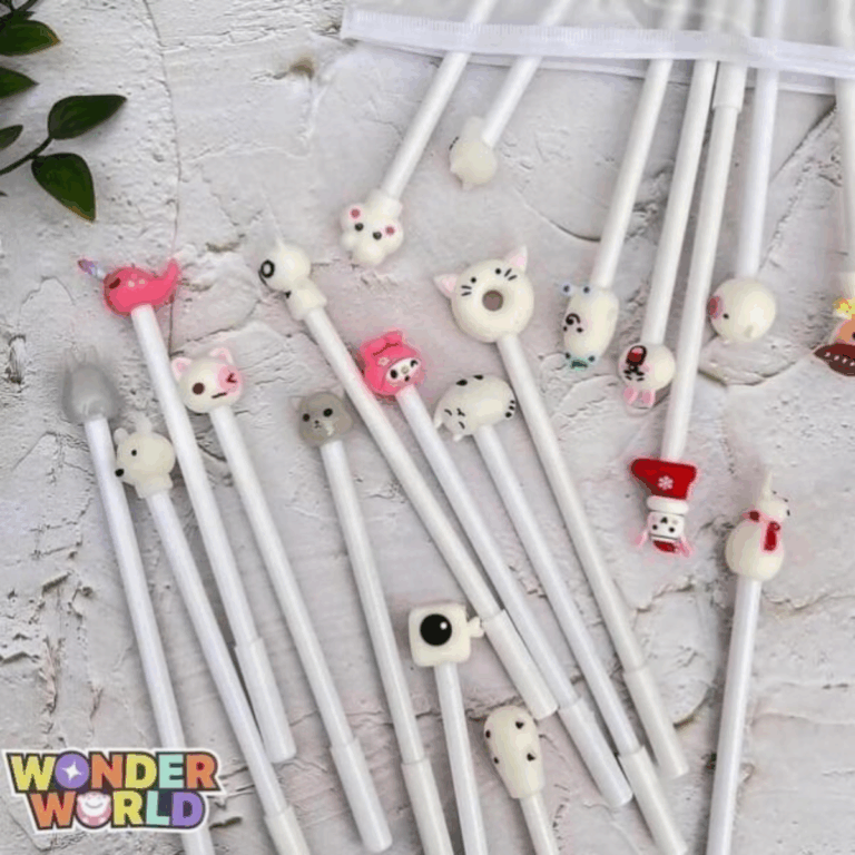 A lovely arrangement of cream-white gel pens, each decorated with a small, colorful sculpted character topper such as a tiny pink narwhal, a sleeping kitty, and a miniature holiday stocking