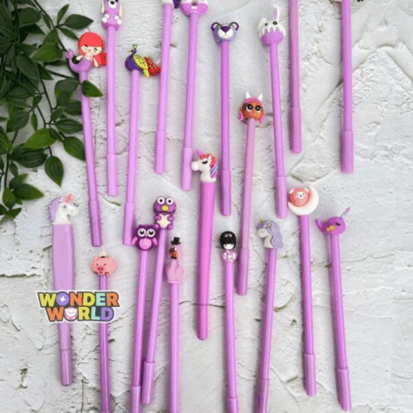 A flat-lay showcase of pastel lavender gel pens arranged on a rustic white textured surface with a touch of green foliage, each pen adorned with a whimsical 3D silicone topper featuring various cute characters like a smiling mermaid, a regal peacock, a tiny piglet, and sleeping dreamland creatures