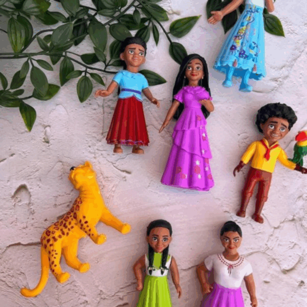 A flat-lay arrangement of seven beautifully sculpted play figurines on a white textured background, featuring beloved characters in vibrant dresses of lilac, magenta, cerulean blue, and lime green, displayed alongside a spotted yellow jaguar and leafy green vines