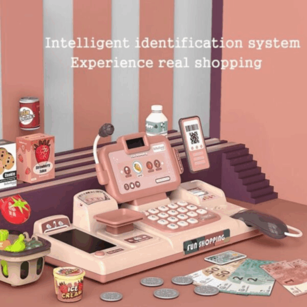 A high-end interactive toy checkout terminal in soft blush pink, featuring a mock smart display screen, cream-colored buttons, and a dark plum barcode scanner, displayed with play money, miniature grocery replicas, and a small shopping basket