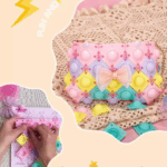 A close-up display of a DIY pastel-colored pop-it purse constructed from interlocking diamond panels of pink, lavender, yellow, and mint green, connected with tiny clear-pink joints, featuring a shimmering glitter-tulle pink bow at the center and resting on a textured cream crochet surface next to separate loose pop-it puzzle tiles