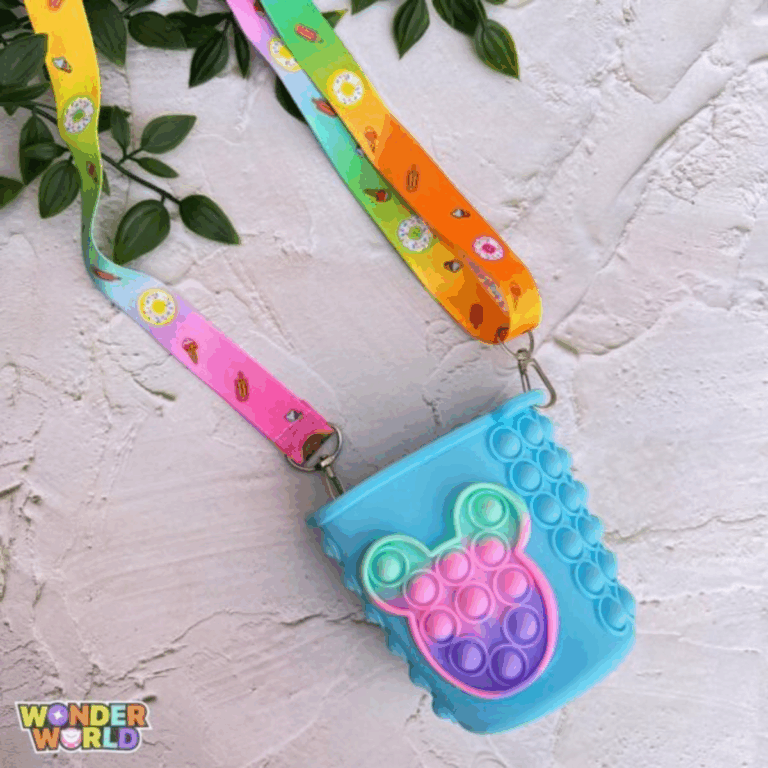 A close-up display of a whimsical cup-shaped silicone pop-it purse in soft sky blue, featuring a front-facing pop-it panel sculpted into an adorable miniature mouse-head silhouette with a vibrant mint green, pink, and purple gradient, complete with a colorful patterned shoulder strap decorated with tiny sweet treats