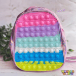 A round mini backpack featuring a metallic, holographic pink vinyl shell and a front pop-it bubble panel in horizontal rows of pink, lavender, mint blue, white, royal blue, and neon yellow-green