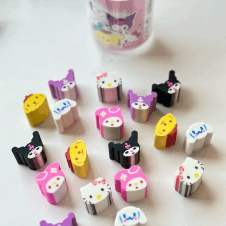 A scattering of colorful, miniature die-cut rubber erasers shaped like Sanrio character heads, showcasing Hello Kitty, Cinnamoroll, My Melody, Pompompurin, and Kuromi in both purple and black hoods, set against a clean white surface with a soft-focus clear plastic tub in the background