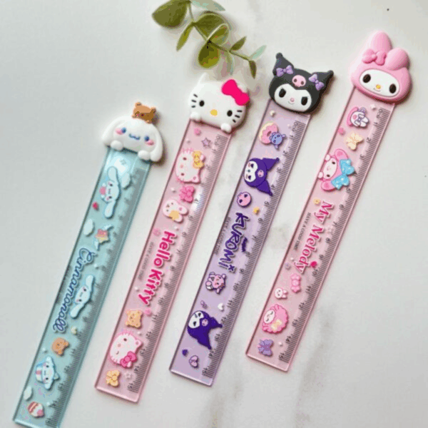 A flat-lay display of four colorful translucent acrylic rulers resting on a light marble surface next to a small green leafy branch, each featuring a large 3D silicone character head topper and color-coordinated themed prints along the body, showcasing Cinnamoroll with a tiny brown bear in mint blue-green, Hello Kitty in pastel pink, Kuromi in translucent purple, and My Melody in rose pink