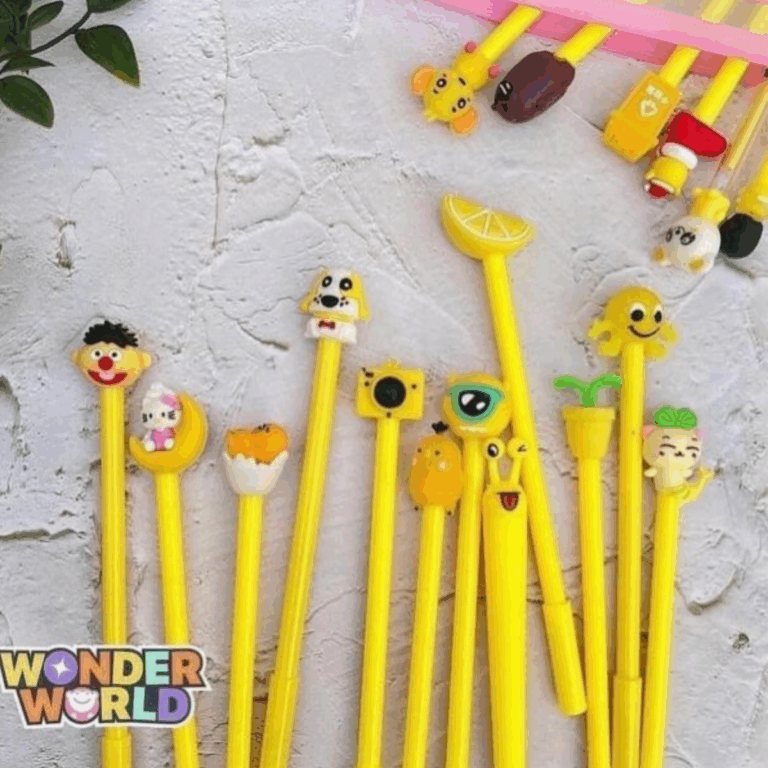 A vibrant collection of bright yellow gel pens spread across a textured surface, each capped with a unique, playful 3D silicone character, including a lemon slice, a puppy, a camera, a silly snail, and a winking kitty resting on a crescent moon