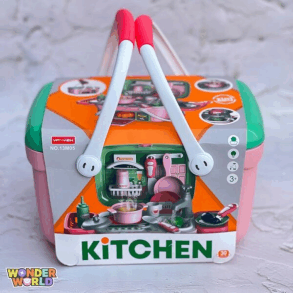 A structured play kitchen basket featuring a soft rose-pink base, a contrasting jade-green lid, and dual curved white handles topped with vibrant coral-red hand grips, shown packaged in an illustrated sleeve