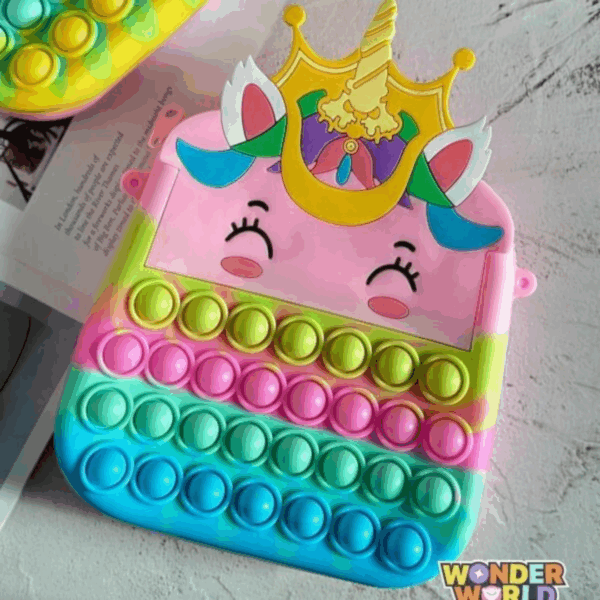 A unicorn-shaped silicone pop-it purse featuring a pastel pink face with sleeping eyes, a sculpted golden crown and horn, and rows of colorful pop-it bubbles in a yellow, pink, and blue gradient