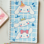 A light blue grid-patterned spiral notebook featuring three cute illustrations of Cinnamoroll stacked vertically, each wearing a different accessory: a party hat, a golden crown, and a pink bow