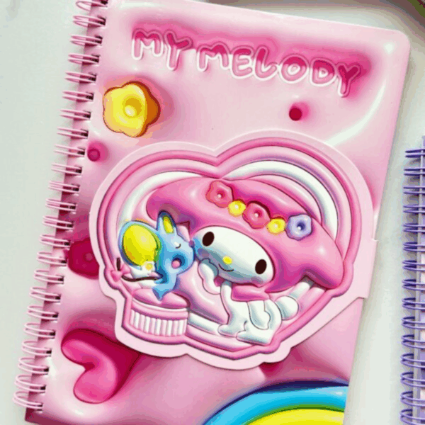 A bubblegum pink spiral notebook featuring a puffy, 3D-effect design where My Melody wears a floral crown and sits next to her blue mouse friend Flat, framed inside a large heart emblem with a peek of a rainbow at the bottom