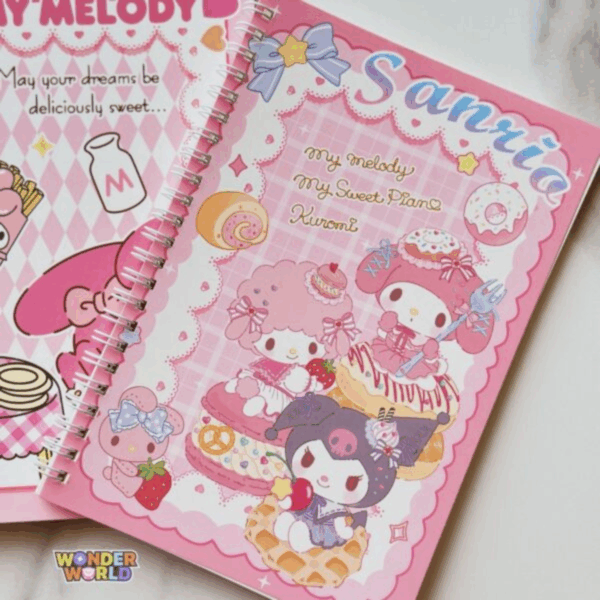 A pink spiral notebook from the file WW604-600x600.jpeg featuring a center panel with a soft pink plaid pattern. It displays My Sweet Piano sitting on a giant macaron, My Melody holding a fork on top of a frosted donut, and Kuromi perched on a waffle, surrounded by a scalloped lace border under the word "Sanrio"