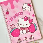 A top-down view of a pink spiral notebook featuring Hello Kitty sitting between large strawberries, wearing a pink polka-dot bow, alongside her teddy bear, small cupcakes, and a boba drink on a checkered pink background