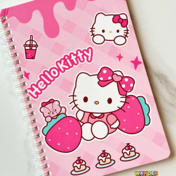 A top-down view of a pink spiral notebook featuring Hello Kitty sitting between large strawberries, wearing a pink polka-dot bow, alongside her teddy bear, small cupcakes, and a boba drink on a checkered pink background